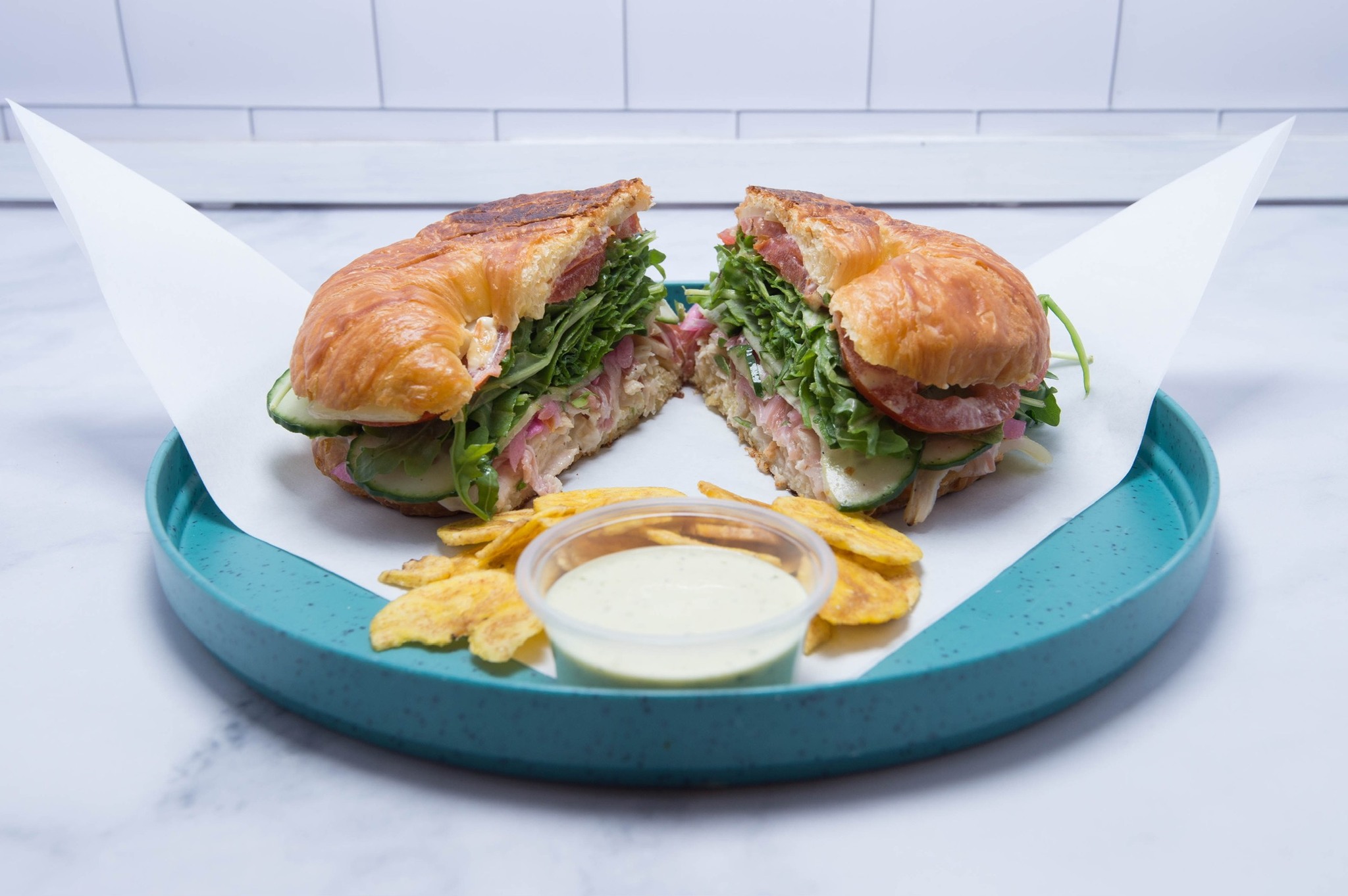 A fresh croissant sandwich on a turquoise plate