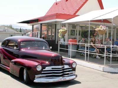 A polished vintage car parked outside Jimmy's red-roofed drive-in while guests sit under the covered patio